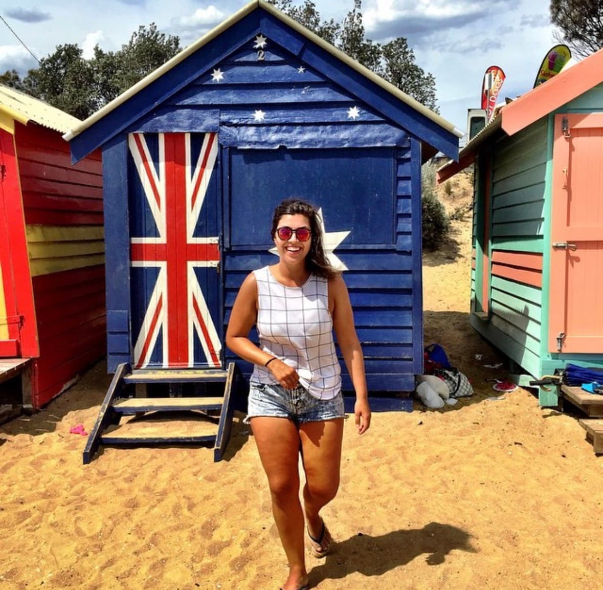 Larissa nas Brighton Beach Bathing Boxes em Melbourne, em frente à casinha com a bandeira australiana — Austrália